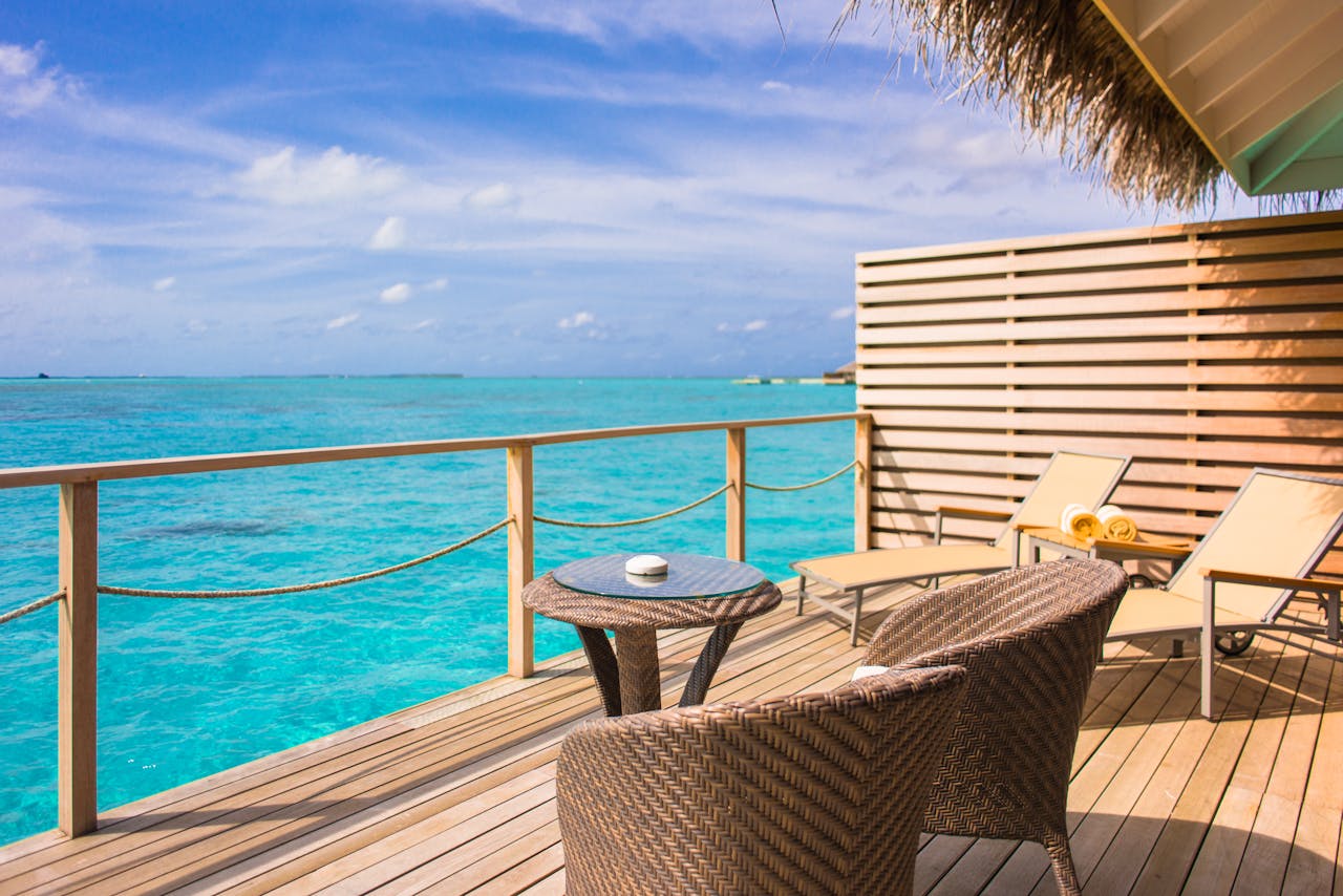Relaxing oceanfront deck with wicker chairs and table, overlooking turquoise waters under blue skies.